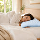Mujer durmiendo de lado sobre una almohada refrescante Pacific Home blanca con patrón celeste en un dormitorio iluminado.