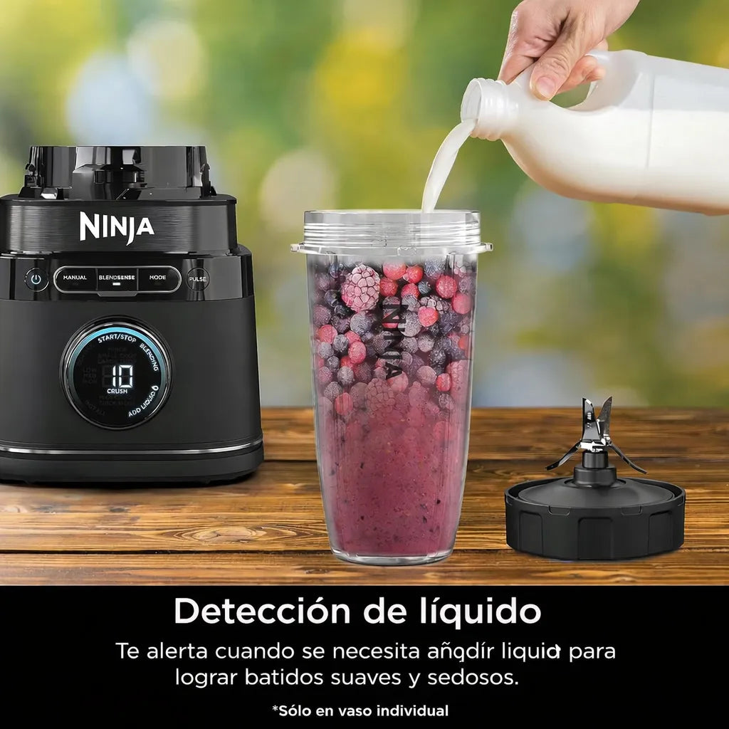 Licuadora Ninja TB301 negra con vaso individual de 24 onzas lleno de frutas congeladas mientras se agrega leche, mostrando la función de detección de líquido para batidos suaves.