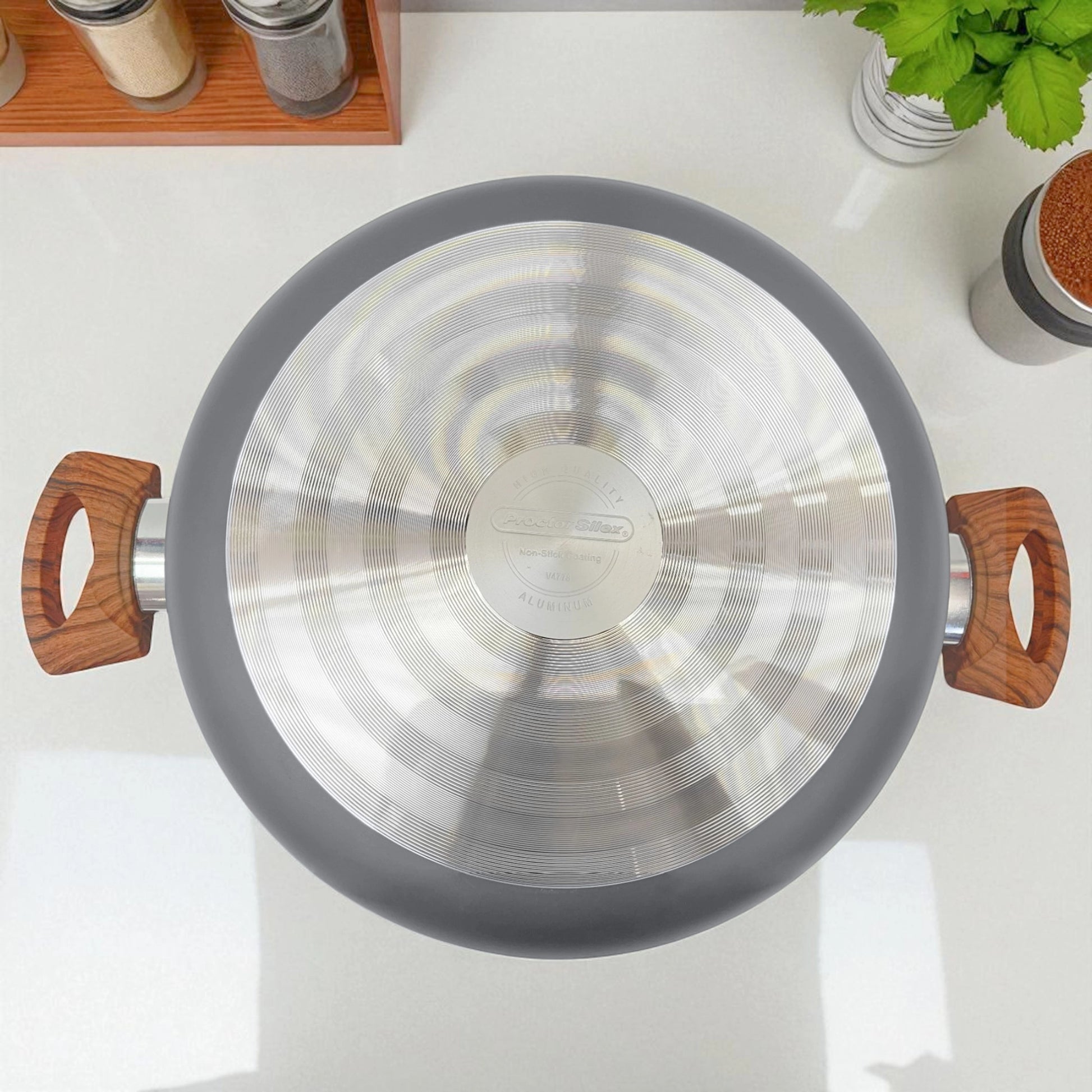 Vista superior de la olla Proctor Silex de 3.5QT mostrando la base de aluminio rayada y mangos efecto madera sobre encimera blanca.