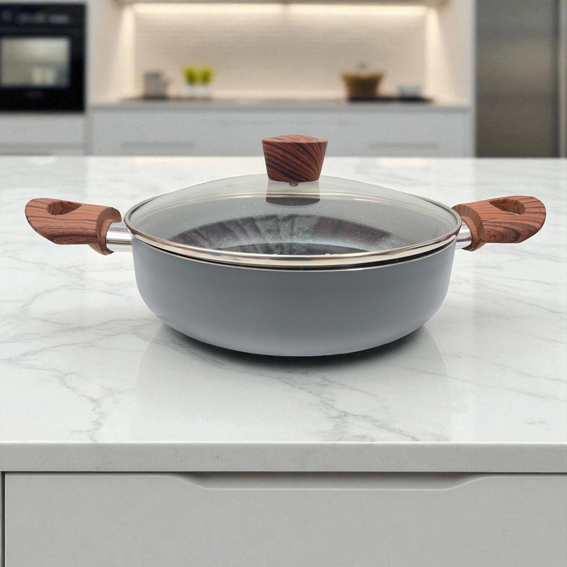 Olla baja Proctor Silex de 3.5QT con tapa de vidrio cerrada, cuerpo gris y mangos efecto madera, mostrada de frente en una cocina moderna.