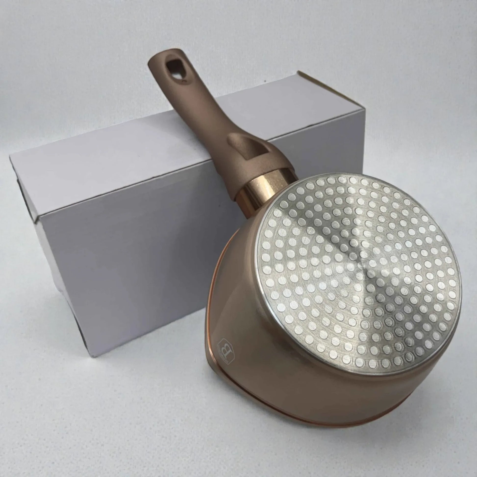 Vista inferior de olla con mango Berlinger Haus Rosegold BH-1224N de 16 x 7.5 cm, mostrando base metálica apta para inducción, cuerpo exterior rosegold y mango largo, apoyada junto a caja blanca.