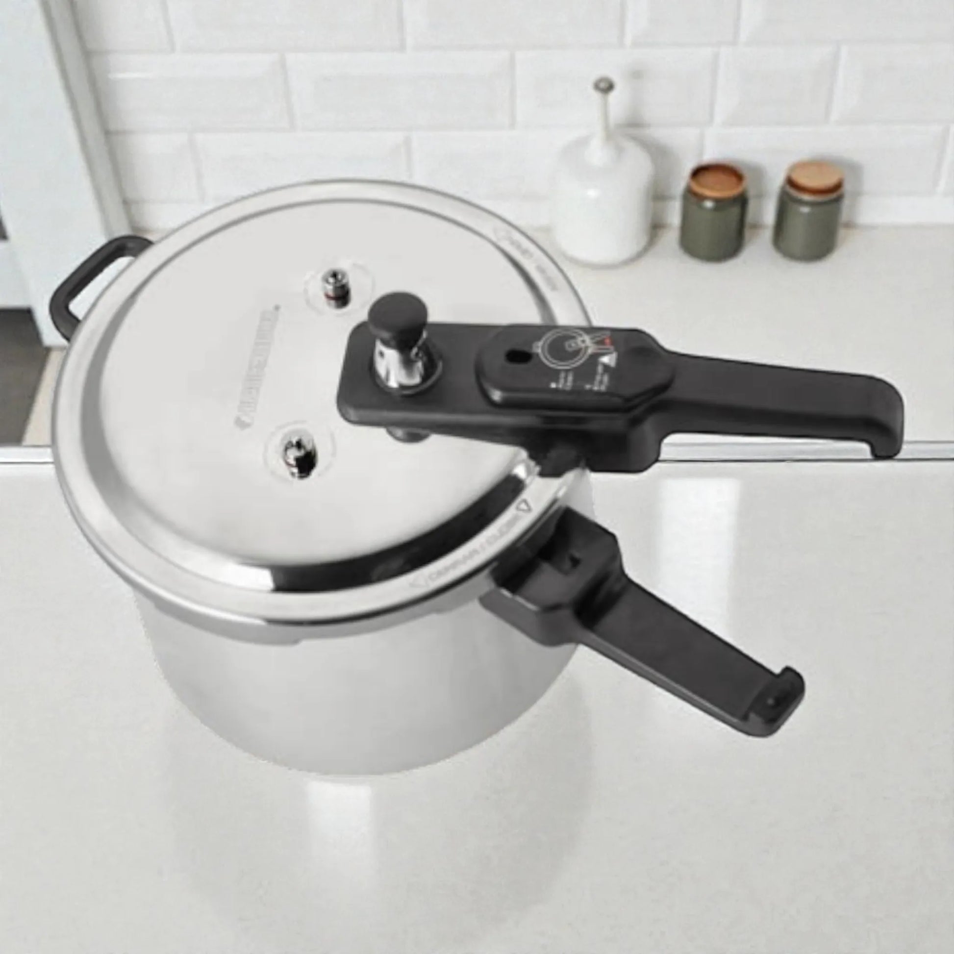 Vista superior de la olla de presión Black+Decker PC700 de 7 litros, tapa plateada con válvulas de seguridad y regulador de presión, manija negra y asa lateral.