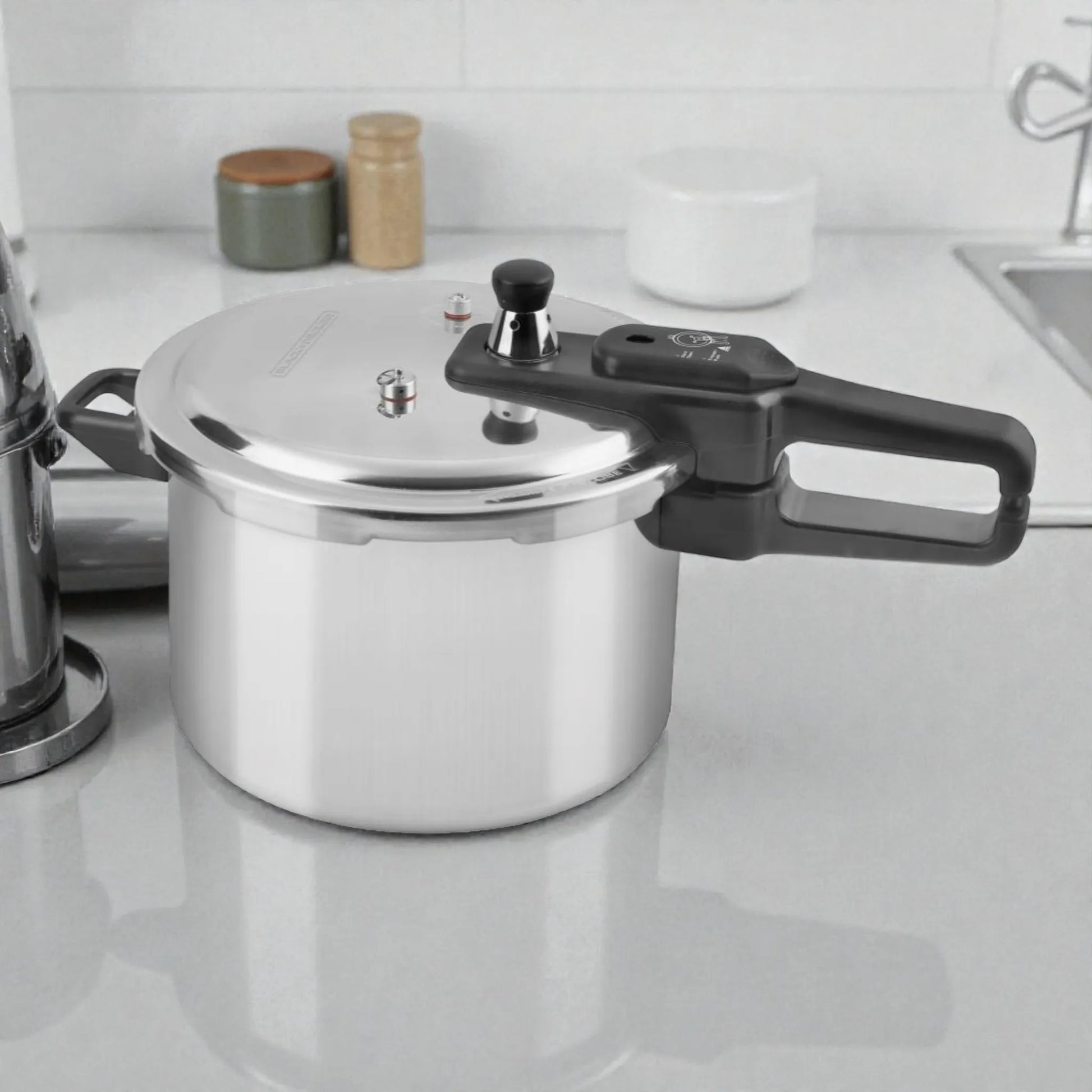 Olla de presión Black+Decker PC700 7 litros en aluminio plateado, vista lateral sobre superficie de cocina, con manija negra fría al tacto y tapa con válvulas de seguridad.