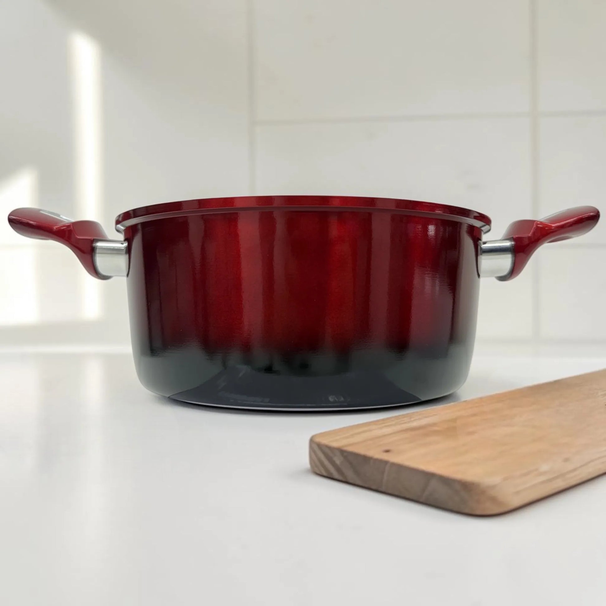 Olla Epicure Escarlata sin tapa en color rojo vino con asas laterales, fotografiada de frente sobre encimera blanca en cocina moderna.