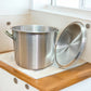 Olla de aluminio industrial de gran capacidad con tapa retirada junto a ventana