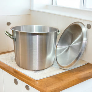 Olla de aluminio industrial de gran capacidad con tapa retirada junto a ventana