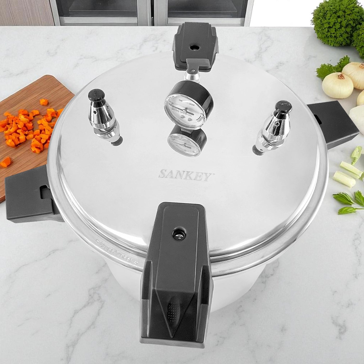 Olla de presión Sankey de 22 litros en aluminio resistente, vista superior con manómetro y asas negras, rodeada de verduras frescas sobre mesa de cocina.