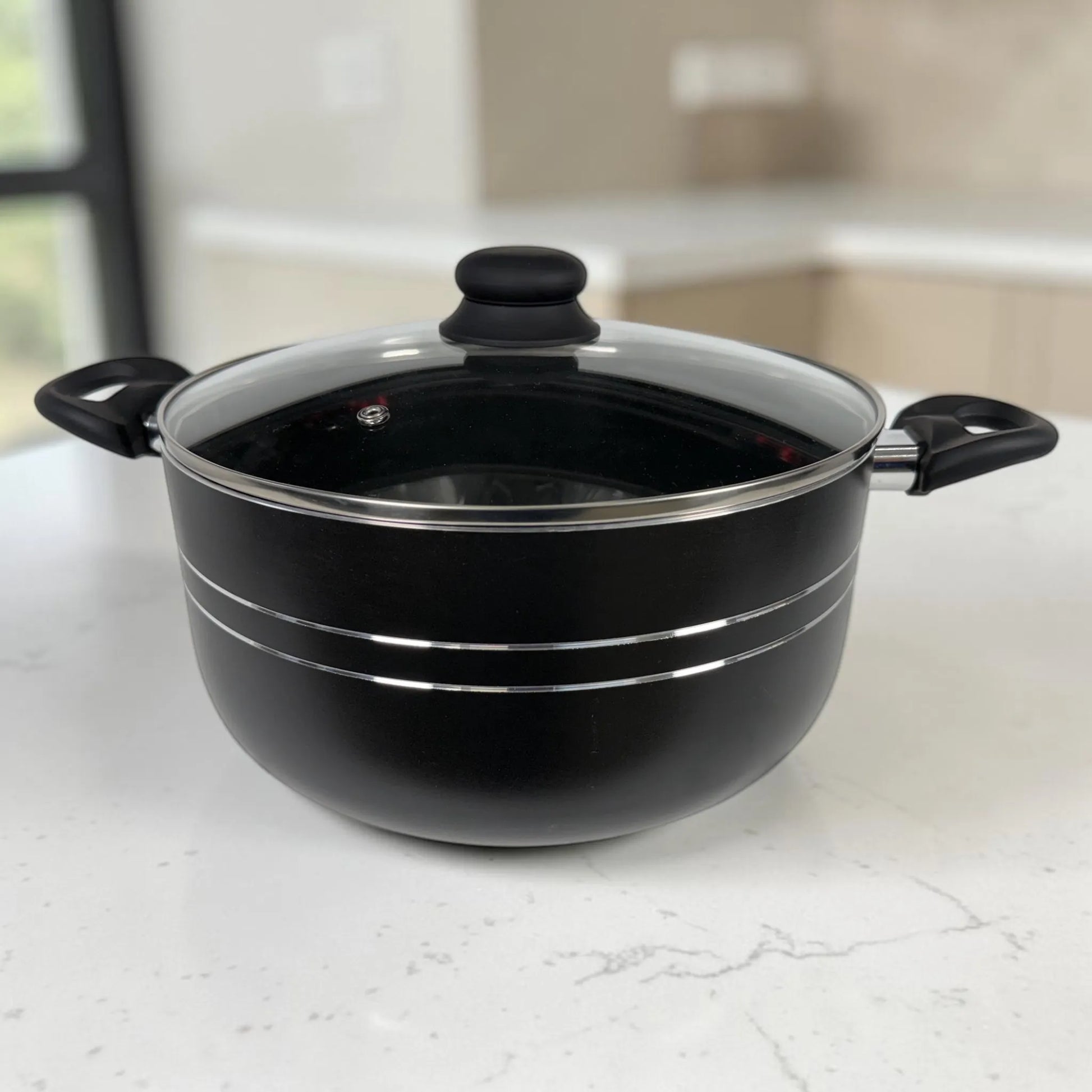 Olla ROCA negra antiadherente con tapa de vidrio, asas laterales y acabado con líneas plateadas.