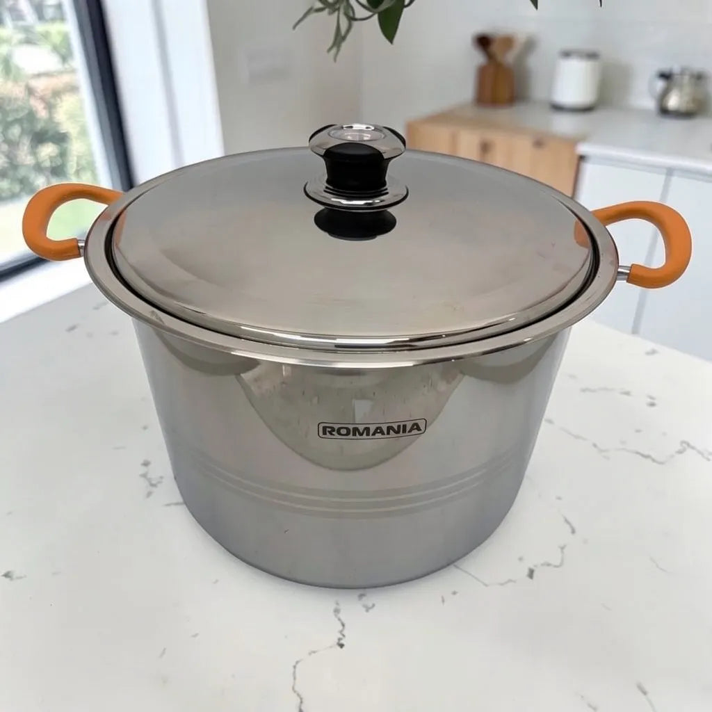 Olla individual Romania de acero inoxidable con tapa metálica y mangos naranjas, fotografiada sobre encimera blanca.