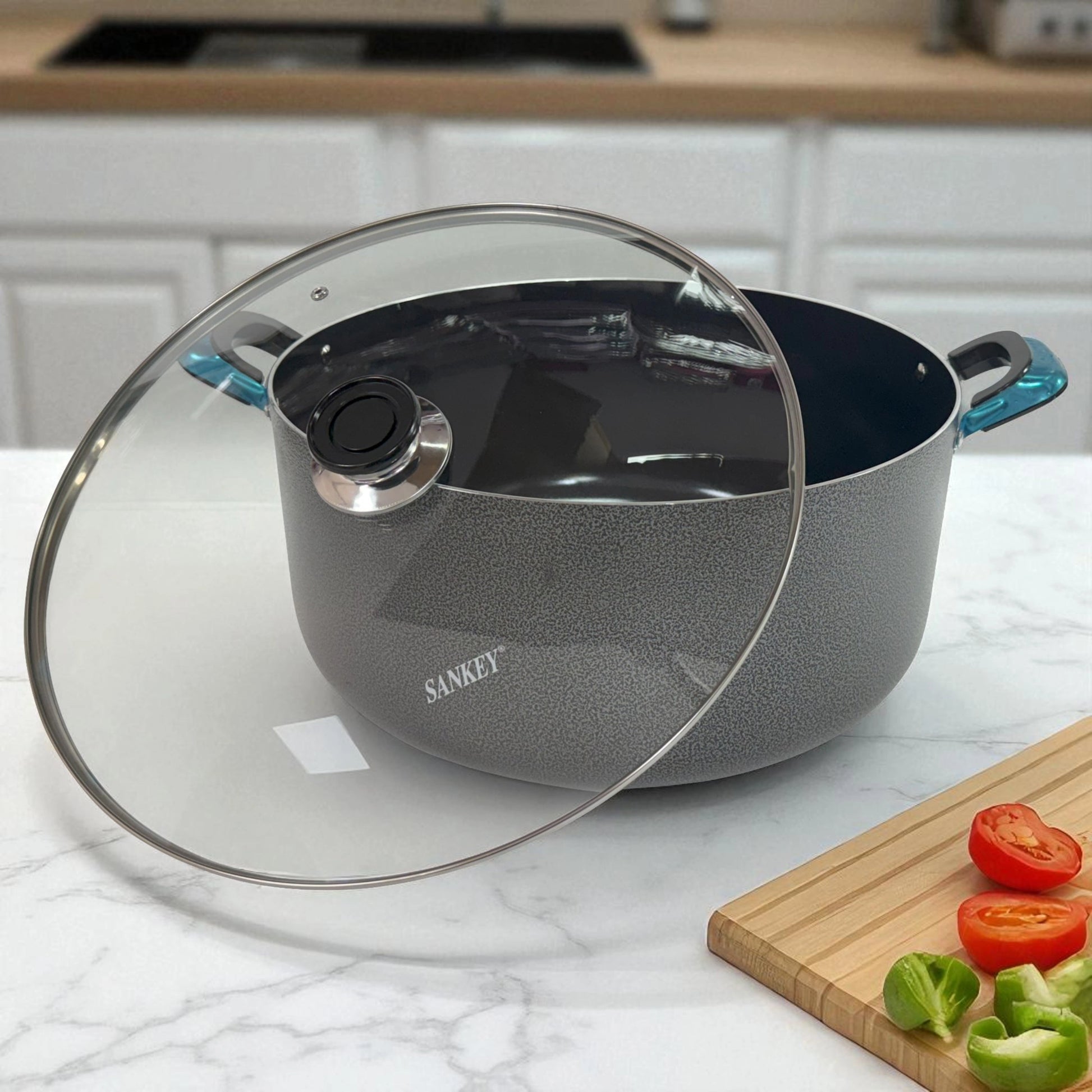 Olla Sankey de 36 cm con tapa de vidrio inclinada, recubrimiento cerámico antiadherente, sobre encimera blanca con vegetales picados