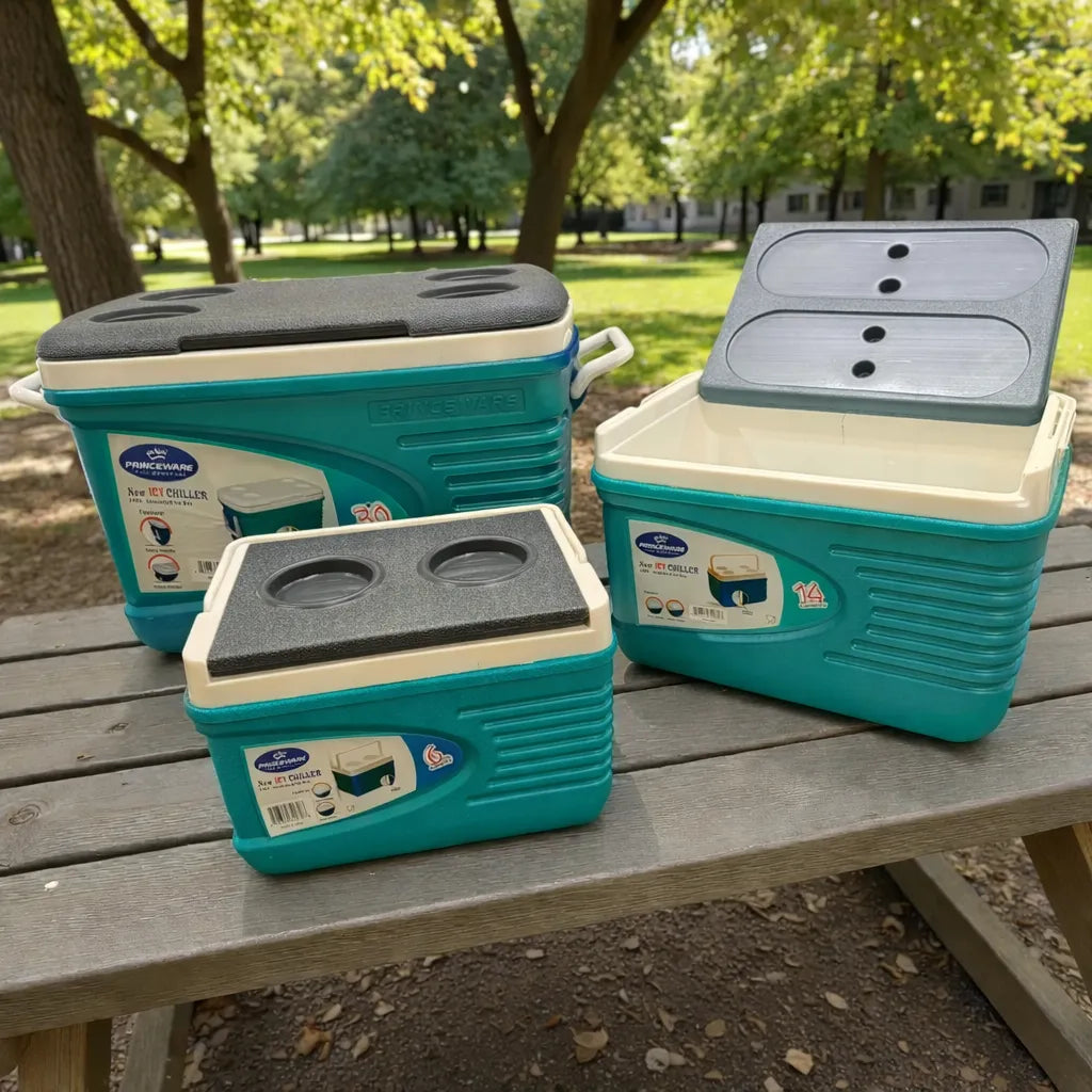 Set de hieleras Princeware New Icy Chiller: hielera 14L con tapa levantada mostrando interior, junto a hielera 30L y 6L en color turquesa con detalles blanco/gris sobre mesa de picnic en parque.