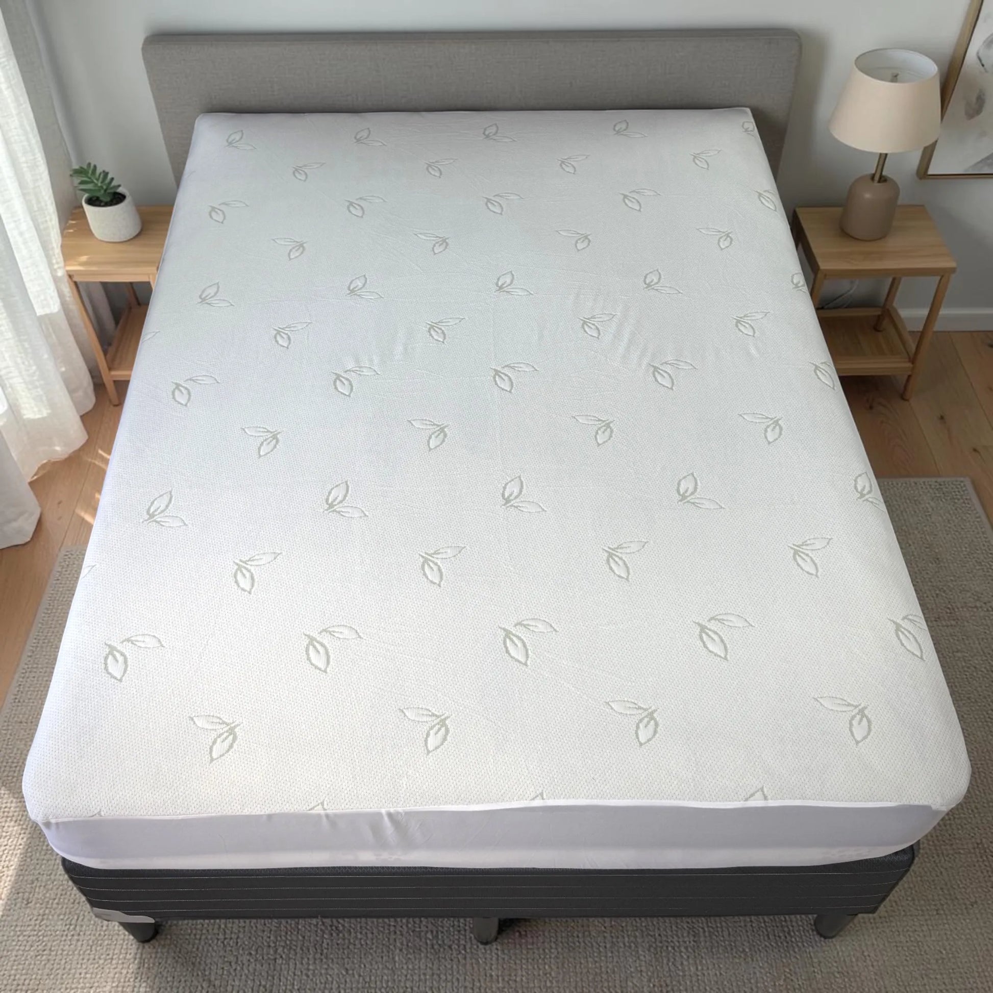 Vista cenital de un protector de colchón impermeable de fibra de bambú, color blanco, cubriendo completamente una cama grande con falda lateral ajustada.