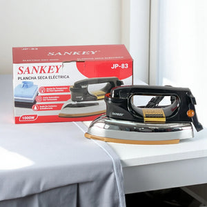 Plancha seca eléctrica Sankey JP-83 de 1000 W en vista frontal 3/4, color negro con cuerpo cromado y suela cerámica dorada, junto a la caja del producto.