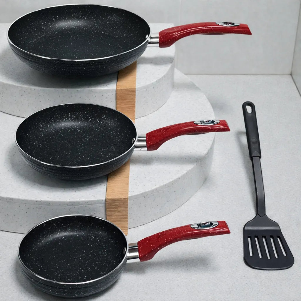Set SANKEY W1626BLG de 3 sartenes antiadherentes (16, 20 y 26 cm) con marble coating negro y mangos rojos, acomodadas en escalones de exhibición; espátula negra decorativa al lado en fondo claro.