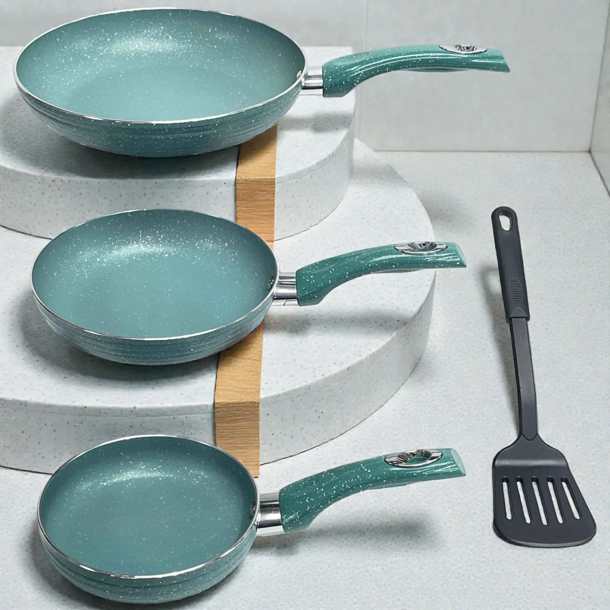 Set de sartenes SANKEY verde turquesa (3 piezas) con recubrimiento antiadherente tipo marble coating, acomodadas en exhibición escalonada; tres sartenes alineadas con mangos hacia la derecha y una espátula negra colocada verticalmente al lado derecho.