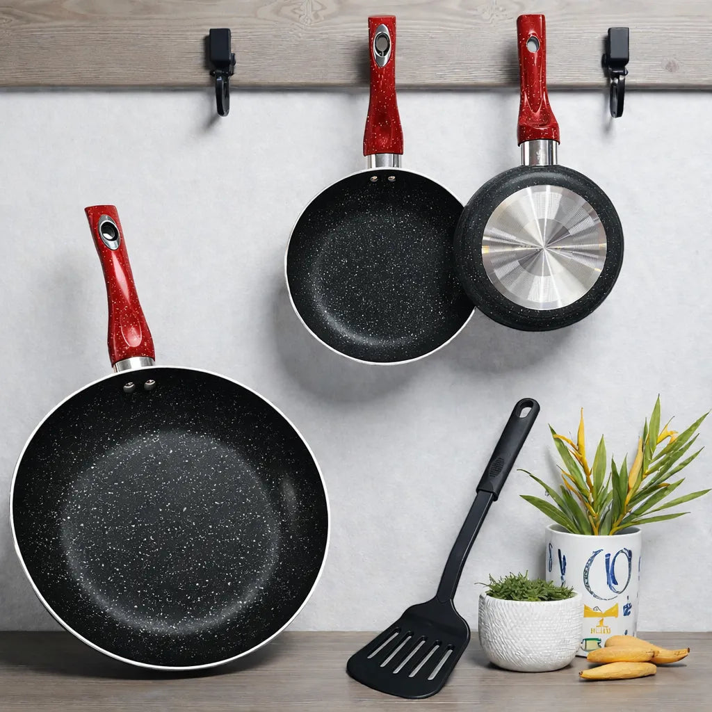 Foto lifestyle del juego de sartenes SANKEY W1626BLG (16/20/26 cm) antiadherentes marble coating con mangos rojos: dos sartenes colgadas y una grande apoyada abajo; una sartén muestra la base metálica, con espátula negra y plantas decorativas.