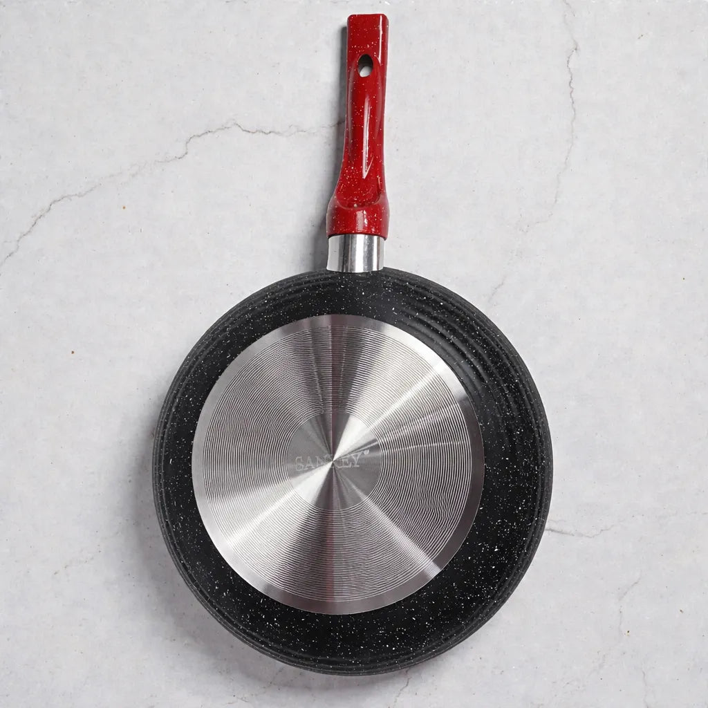 Parte inferior de sartén SANKEY modelo W1626BLG con base metálica circular y cuerpo negro moteado; mango rojo orientado hacia arriba, sobre fondo claro tipo mármol.
