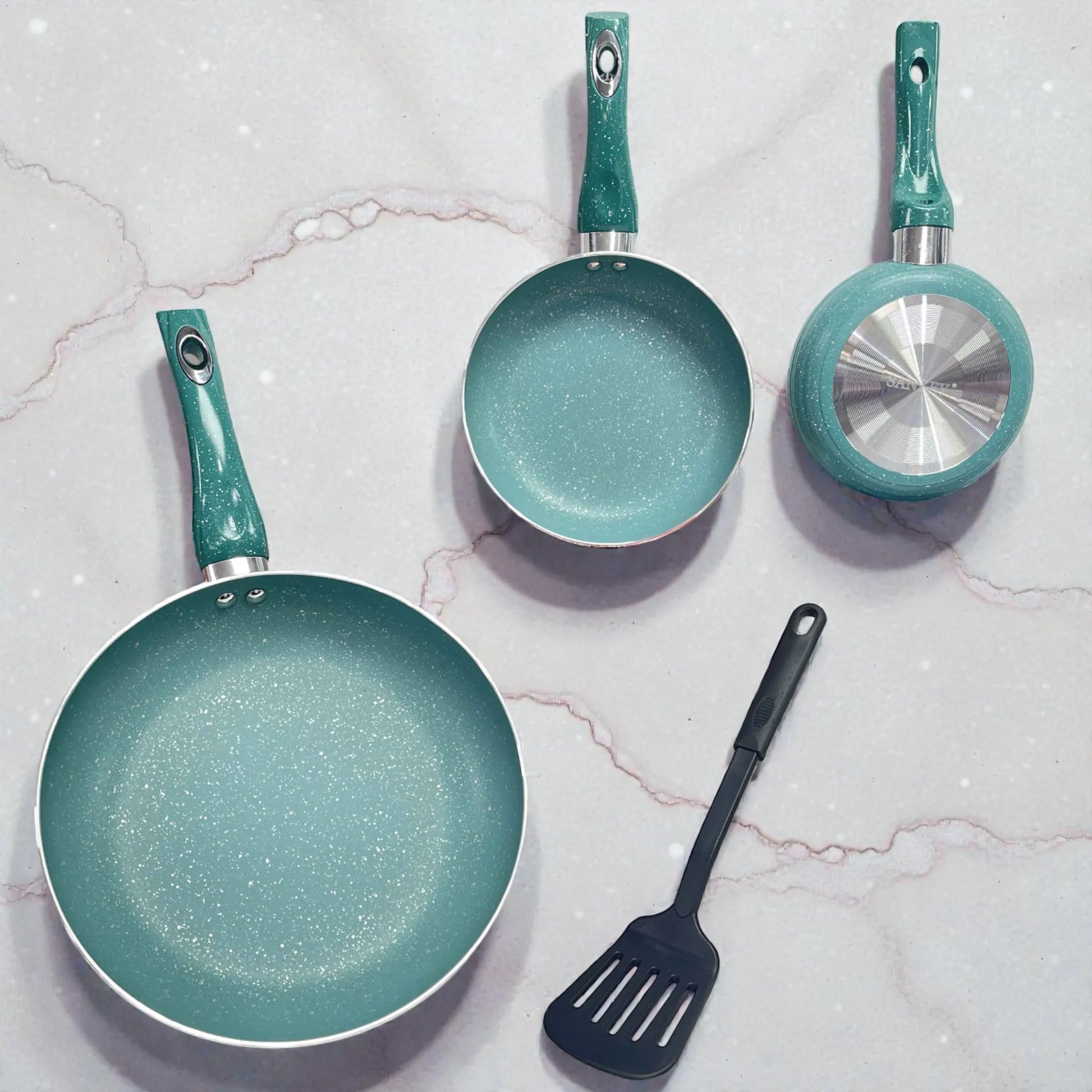 Vista superior flat lay del set de sartenes SANKEY color verde turquesa (3 piezas: 16/20/26 cm) antiadherentes tipo marble coating; se ven dos sartenes por dentro y una volteada mostrando la base metálica circular, junto a una espátula negra sobre fondo tipo mármol.