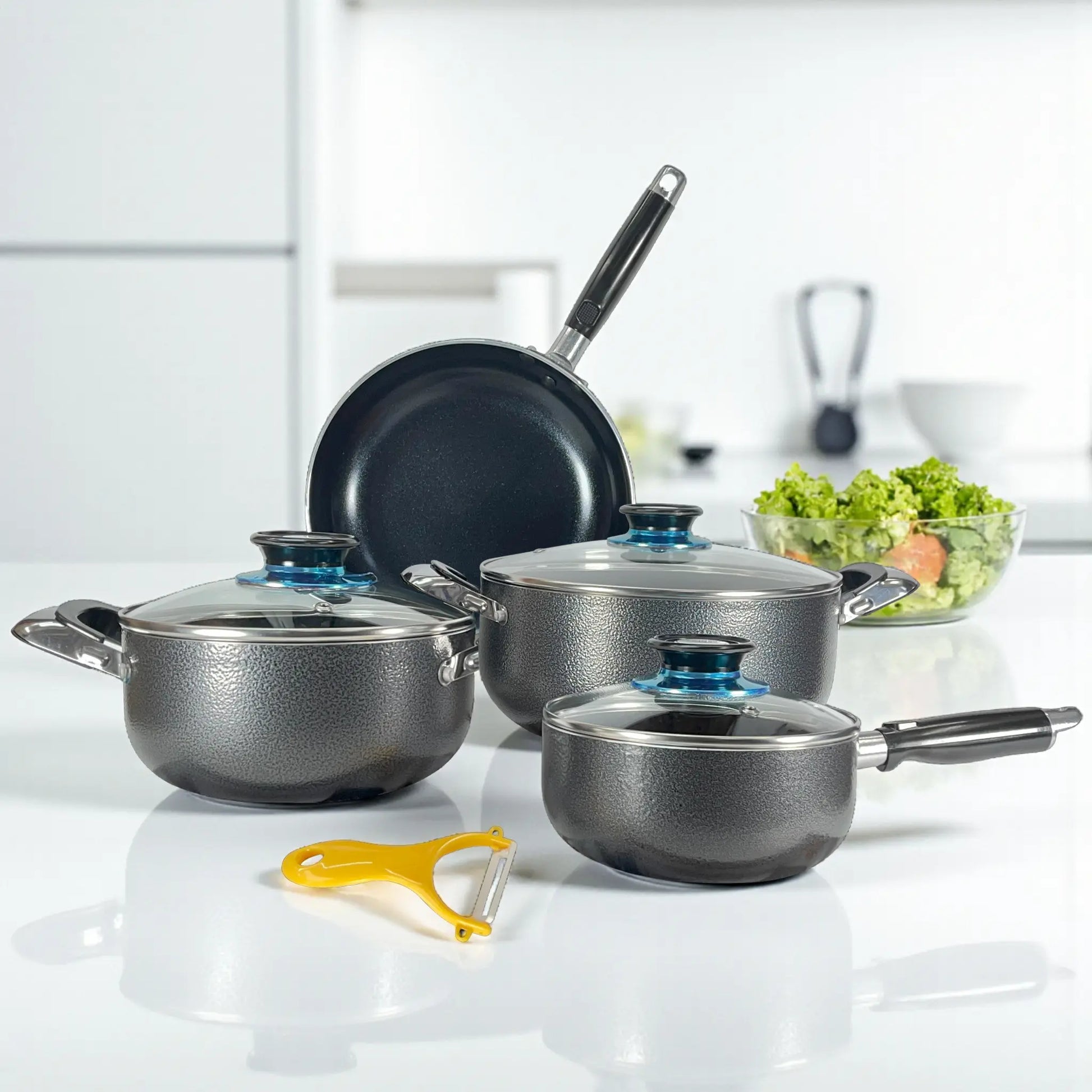 Juego de 7 piezas Sankey W-757 sobre encimera blanca en cocina moderna: sartén 24 cm al fondo, dos ollas 24 y 18 cm con tapas y cacerola 16 cm con mango largo; pelador incluido.