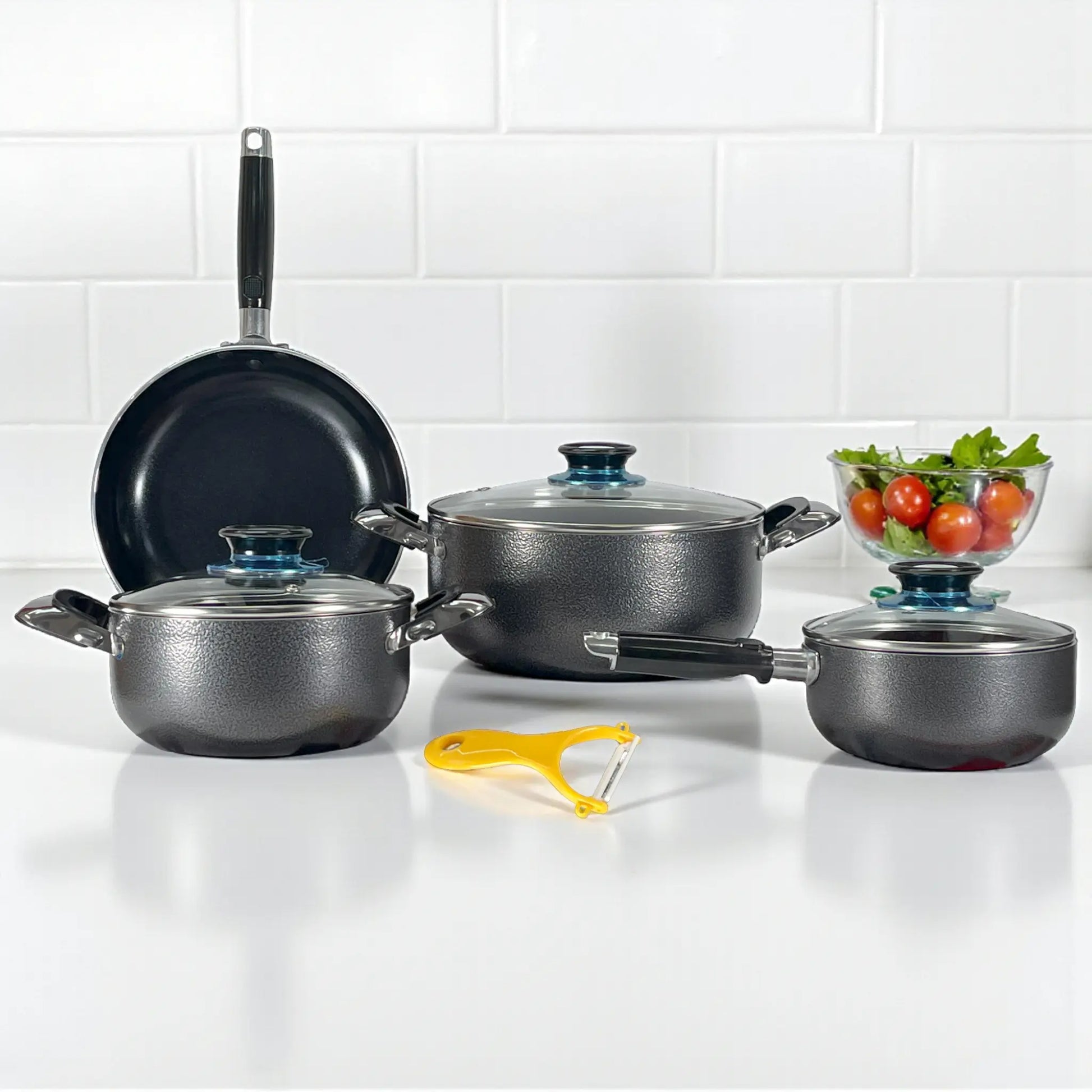 Set Sankey W-757 color gris granito; sartén 24 cm de pie al fondo, olla 24 cm con tapa al centro, olla 18 cm izquierda, cacerola 16 cm derecha; pelador cerámico amarillo al frente.