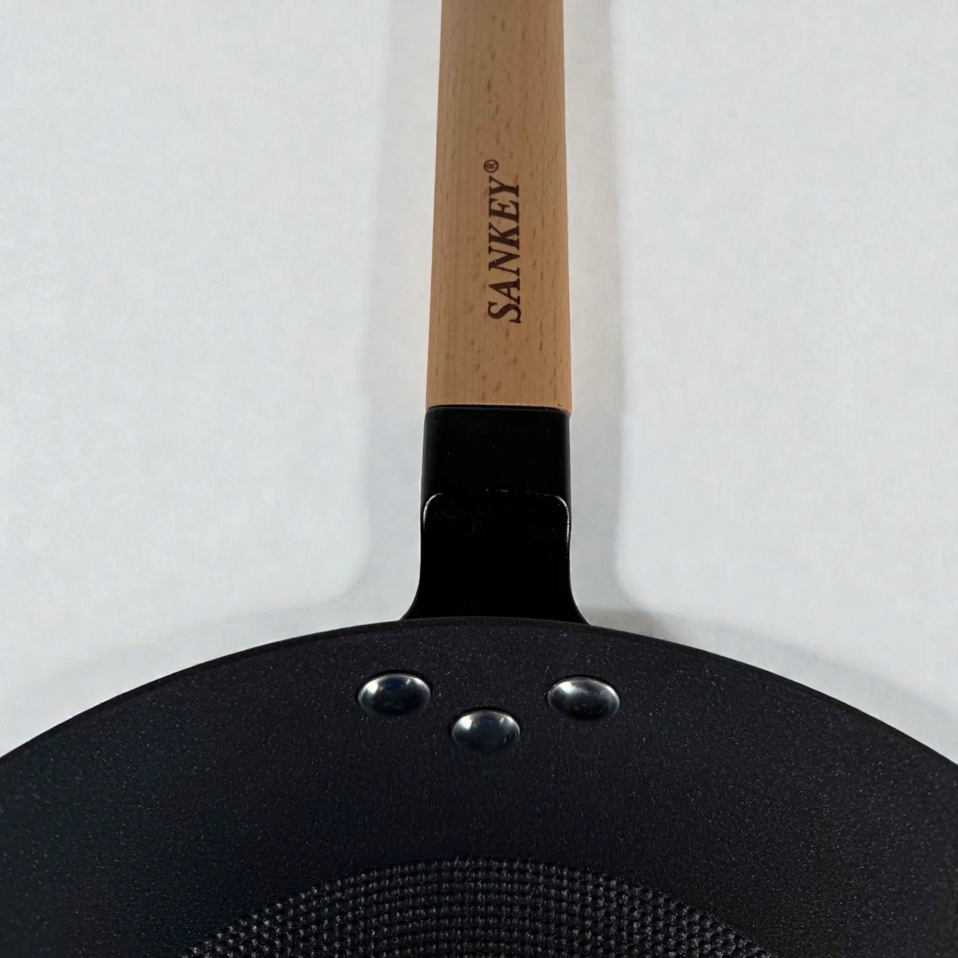 Detalle del mango de madera del wok Sankey de hierro fundido negro 30 cm (12”), mostrando logo Sankey y remaches de sujecion.