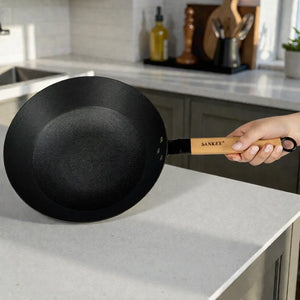 Wok Sankey de hierro fundido negro de 30 cm (12 pulgadas) con mango de madera, interior con superficie tipo panal, sostenido con la mano en cocina.