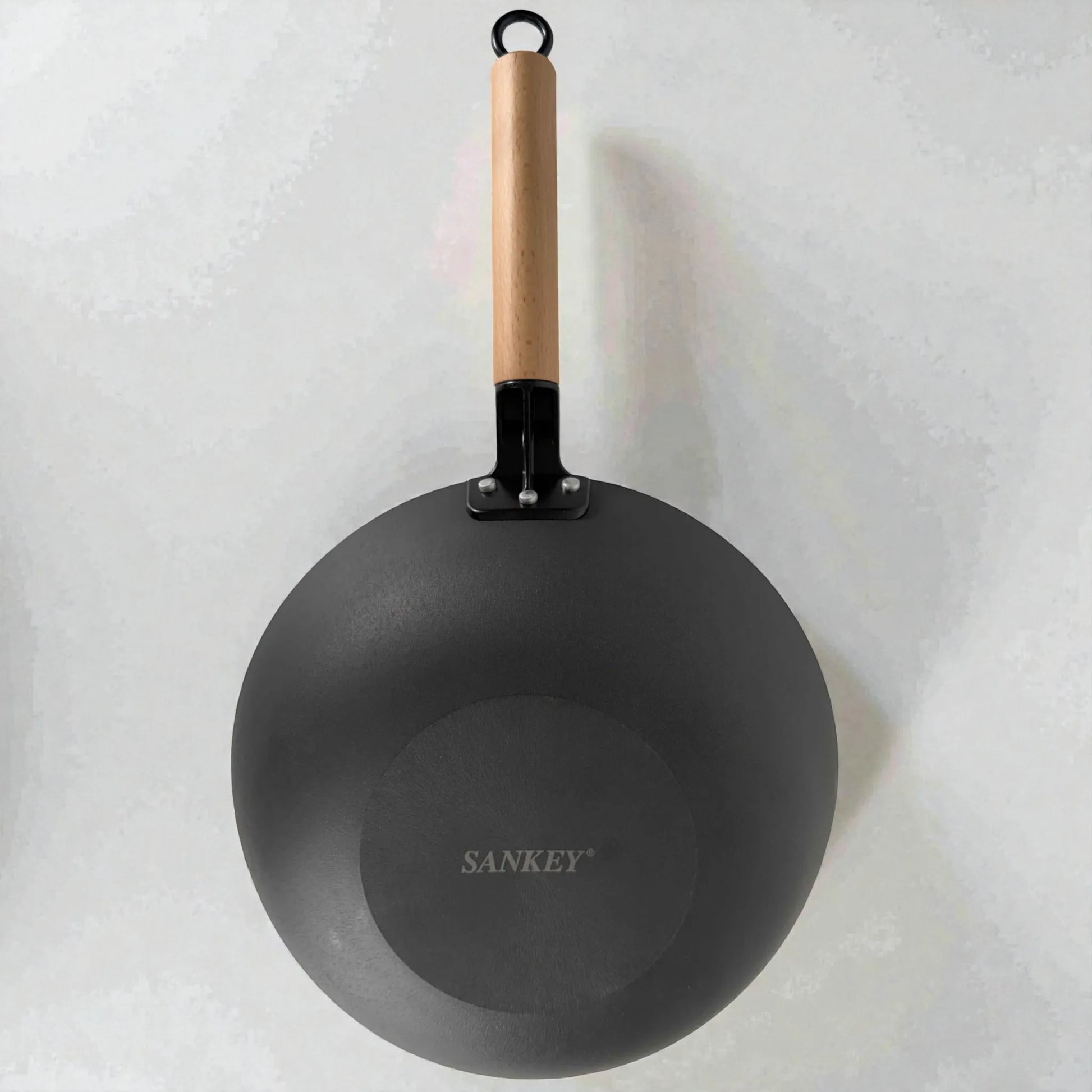 Vista inferior del wok Sankey de hierro fundido negro 30 cm (12 pulgadas), mostrando base exterior con logo Sankey y mango de madera con aro para colgar, sobre fondo blanco.