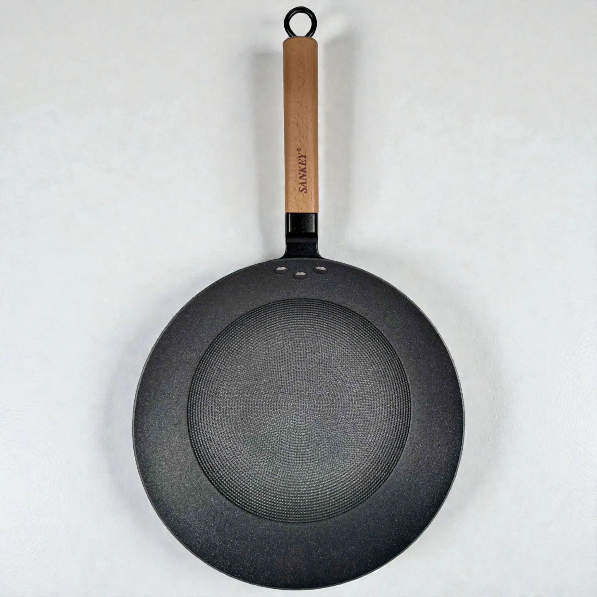 Vista superior del wok Sankey de hierro fundido negro 30 cm (12”), con mango de madera y base interior tipo panal sobre fondo blanco.