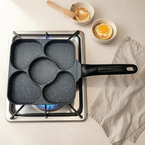 Sarten multifuncional Synamore 5 en 1 de color gris moteado con mango negro, colocado sobre estufa de gas en vista superior, con cinco compartimentos para cocinar huevo, pancakes y desayuno por separado.