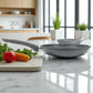 Sartén Big Home gris con mango ergonómico, sobre encimera de cocina moderna junto a tabla con verduras.