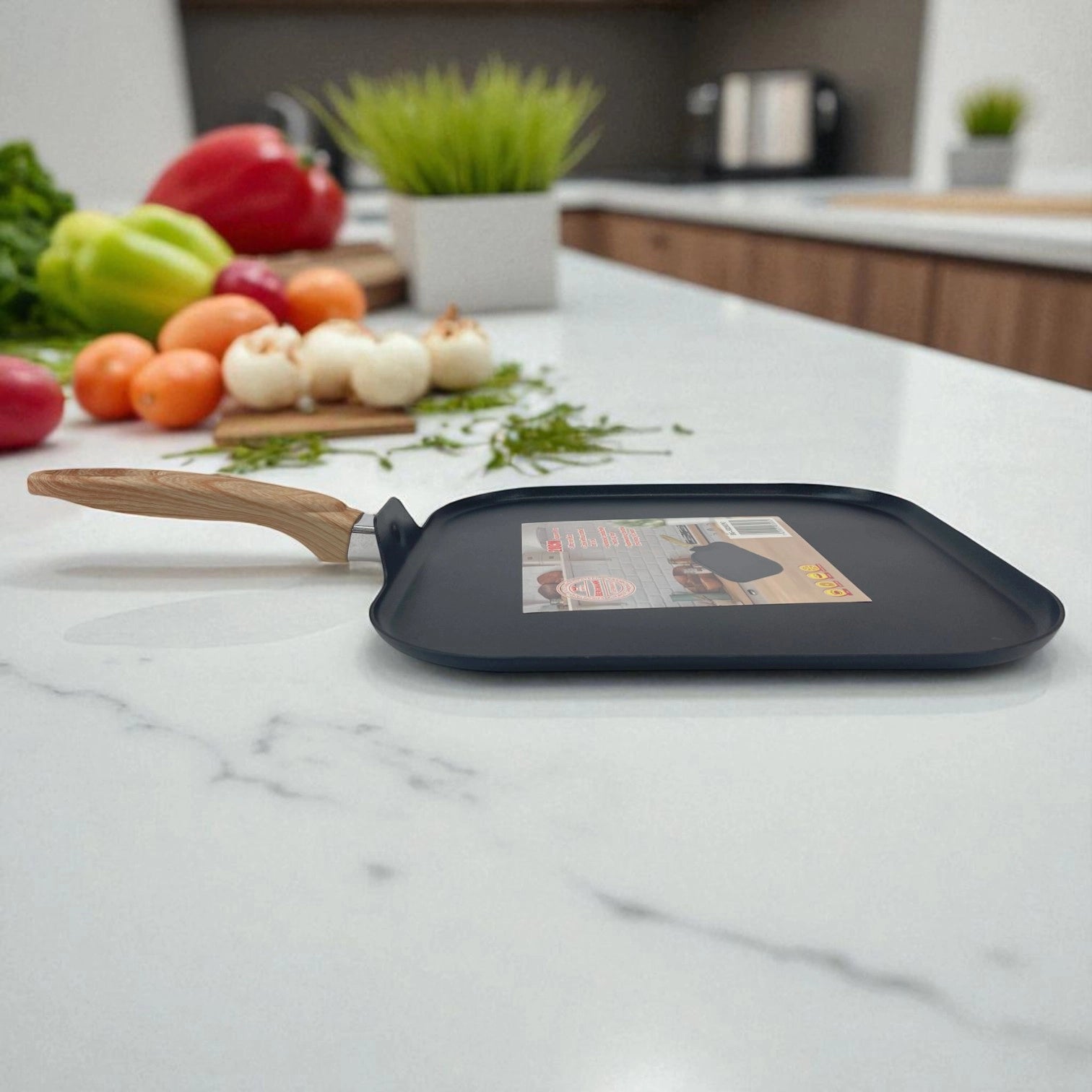 Sartén cuadrado de 28 cm Bergmann con mango de imitación madera, vista lateral sobre encimera de cocina moderna con vegetales al fondo.