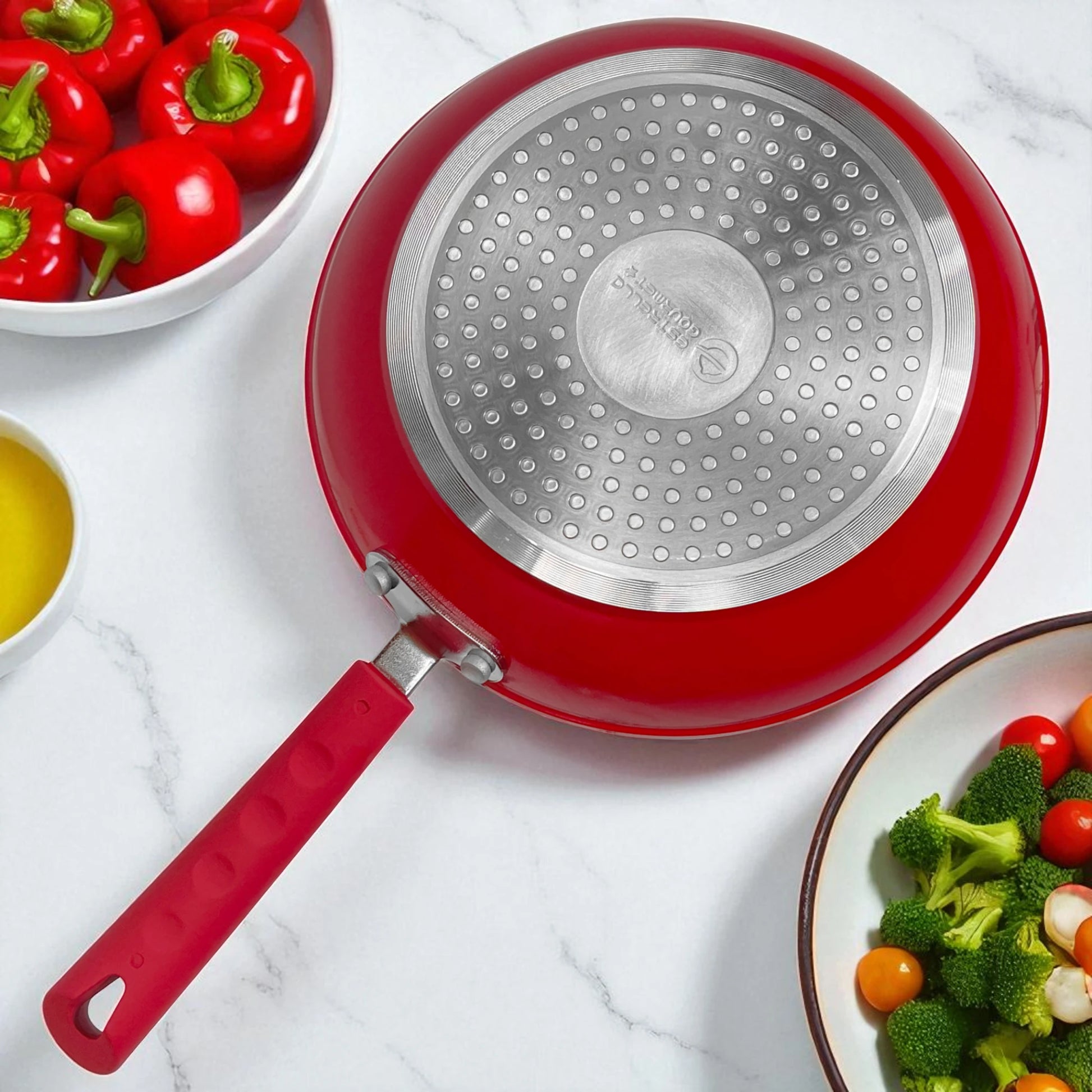 Parte inferior del sartén Estrella Gourmet rojo con base de inducción en acero inoxidable y mango ergonómico de baquelita.