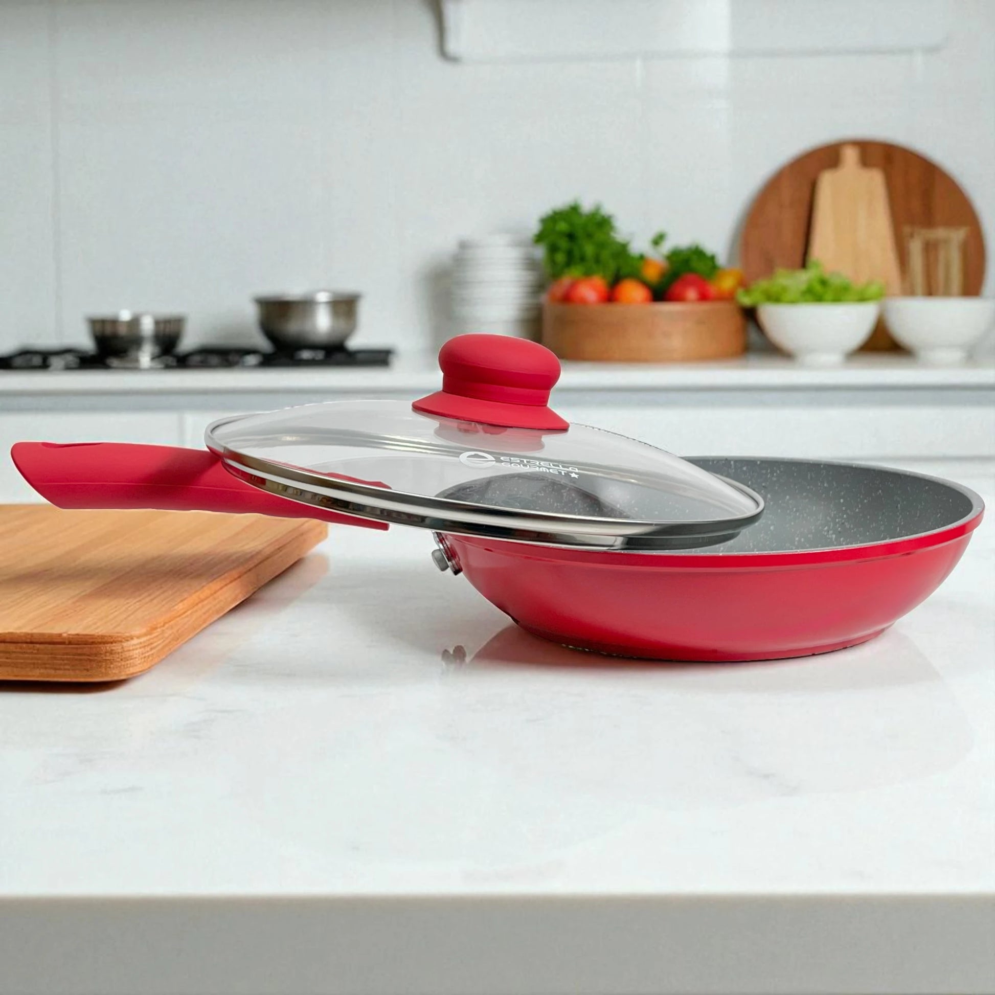 Sartén antiadherente Estrella Gourmet color rojo con tapa de vidrio templado y mango de baquelita resistente al calor sobre mesa de cocina.