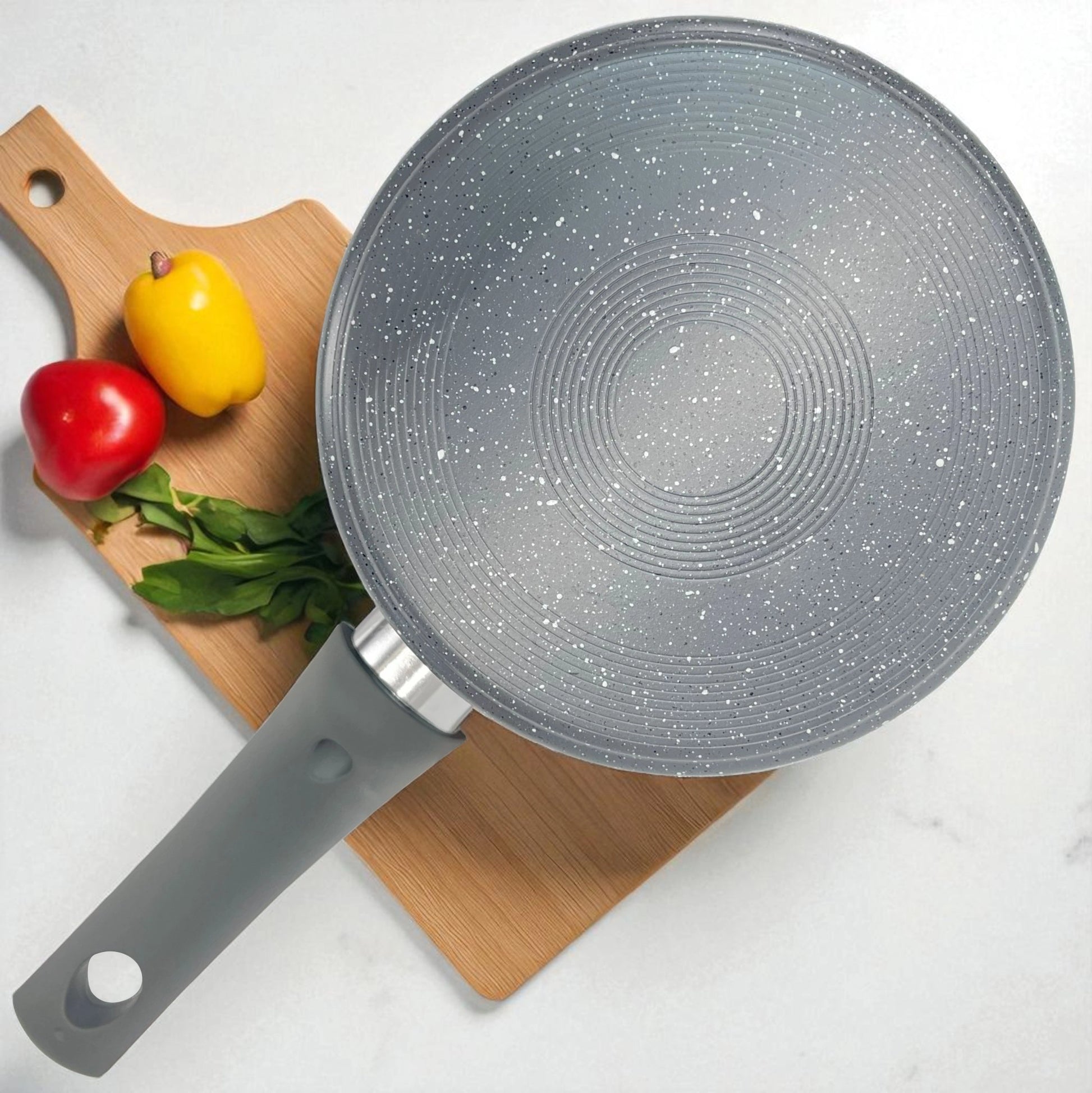 Sartén del set Big Home con acabado granito visto desde arriba, sobre tabla de cortar con vegetales.