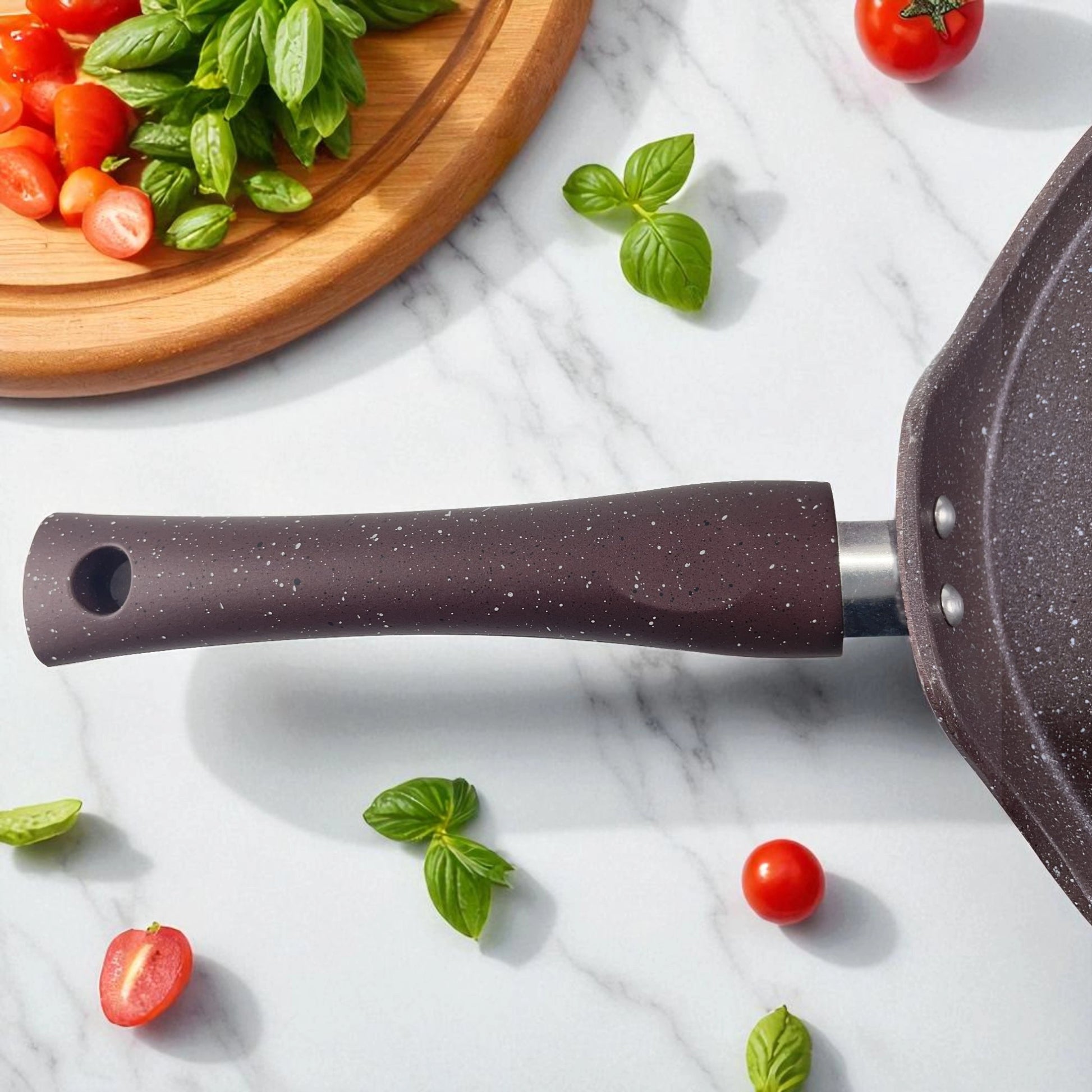 Mango ergonómico del sartén plano antiadherente Hotchef de 25 cm con recubrimiento de mármol, acompañado de tomates cherry y hojas de albahaca.