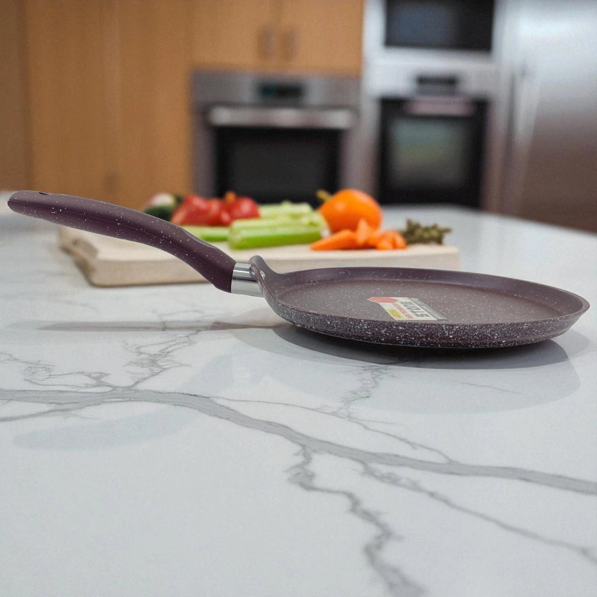 Vista lateral del sartén plano antiadherente Hotchef de 25 cm con recubrimiento de mármol, sobre encimera de cocina con verduras frescas al fondo.