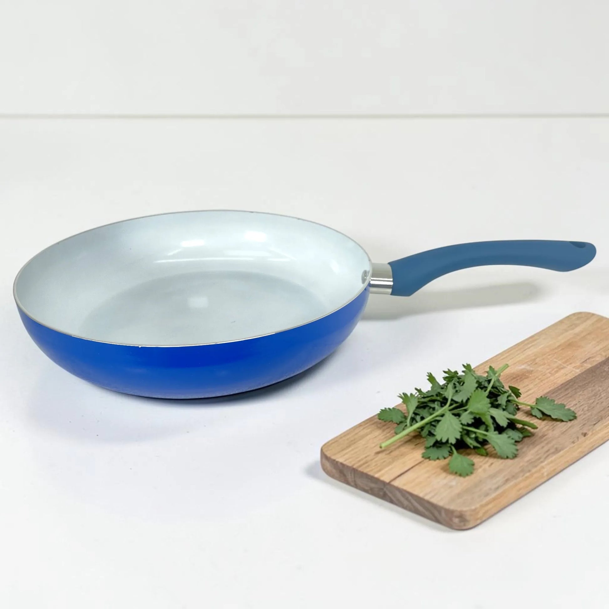 Sartén ROCA azul sin tapa con interior cerámico blanco, mango ergonómico y tabla de cocina decorativa al lado.