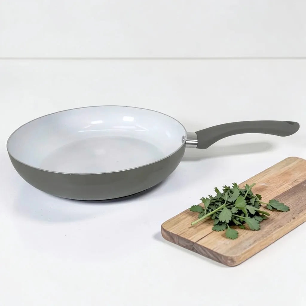 Sartén ROCA gris sin tapa con interior cerámico blanco, mango ergonómico y tabla de cocina decorativa al lado.