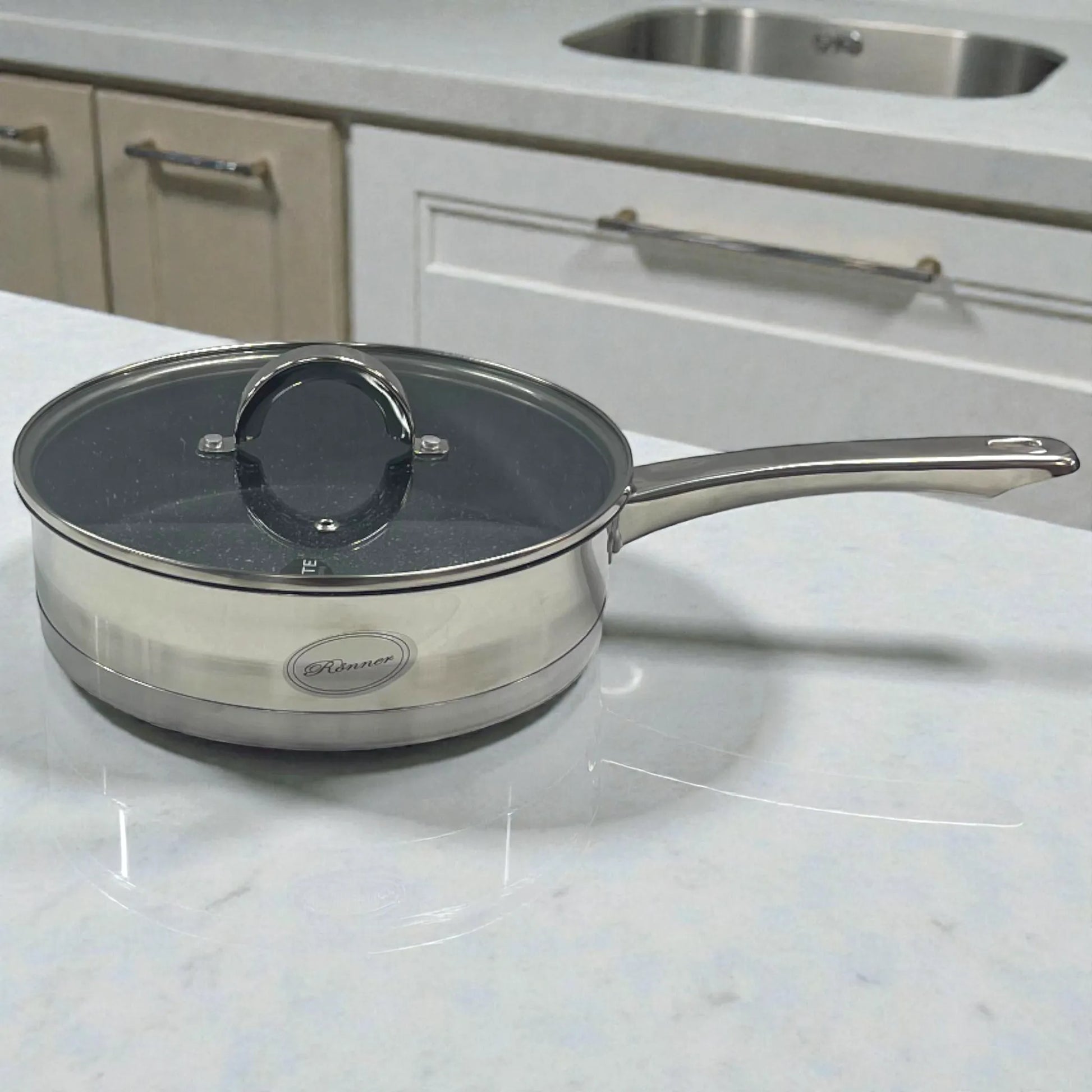 Sartén Rönner Austria de acero inoxidable con tapa de vidrio, tamaño grande, sobre encimera de cocina.
