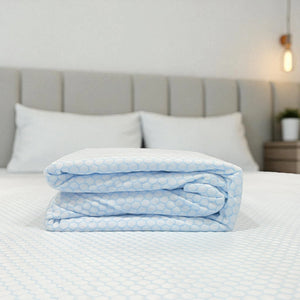 Primer plano del protector Scarlett Classics Cool Sensation plegado, muestra grosor y tejido con panal celeste, hipoalergenico y respirable, en tallas twin, full, queen y king.