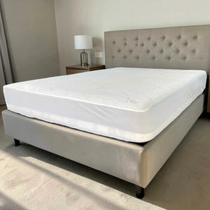 Protector de colchón Scarlett Classics Organic Cotton color blanco, impermeable y ajustable con elástico, instalado en el colchón (vista lateral en dormitorio).