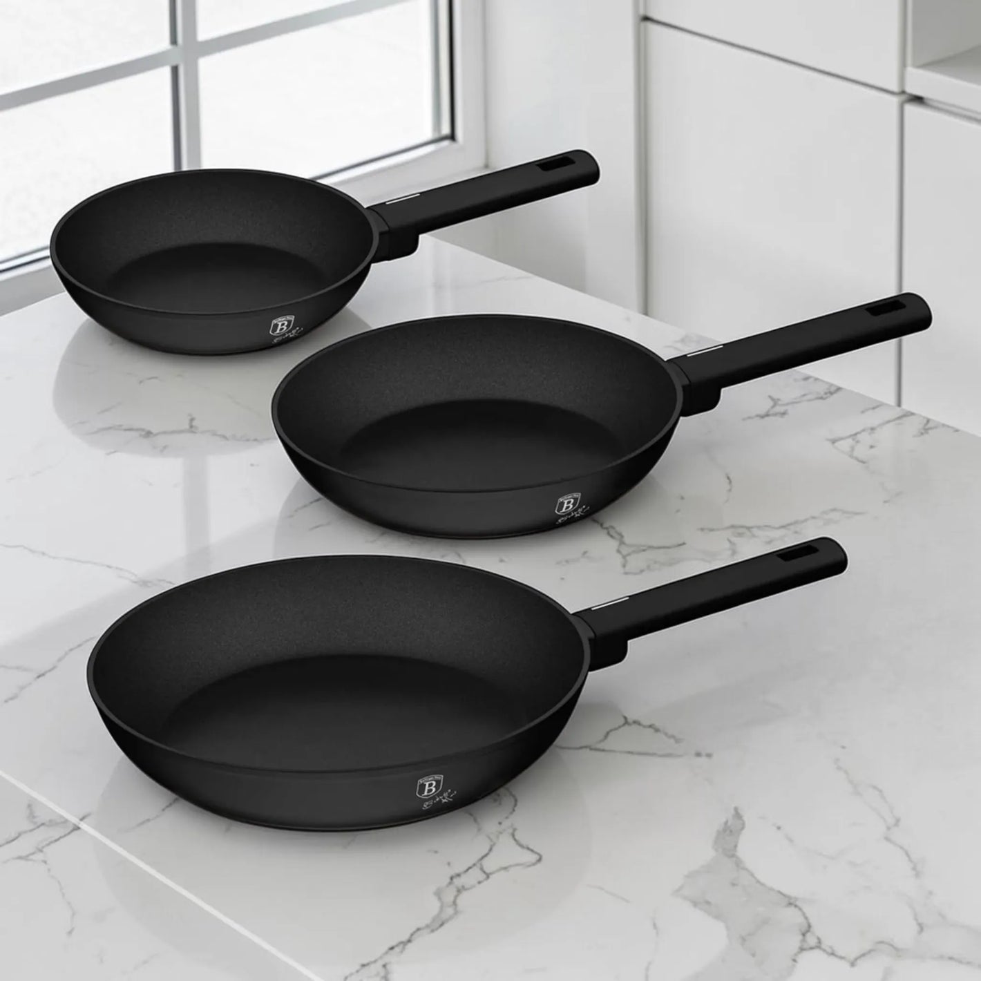 Set de 3 sartenes Berlinger Haus BH-8195A negro mate de 20, 24 y 28 cm sobre cocina moderna con superficie de mármol.