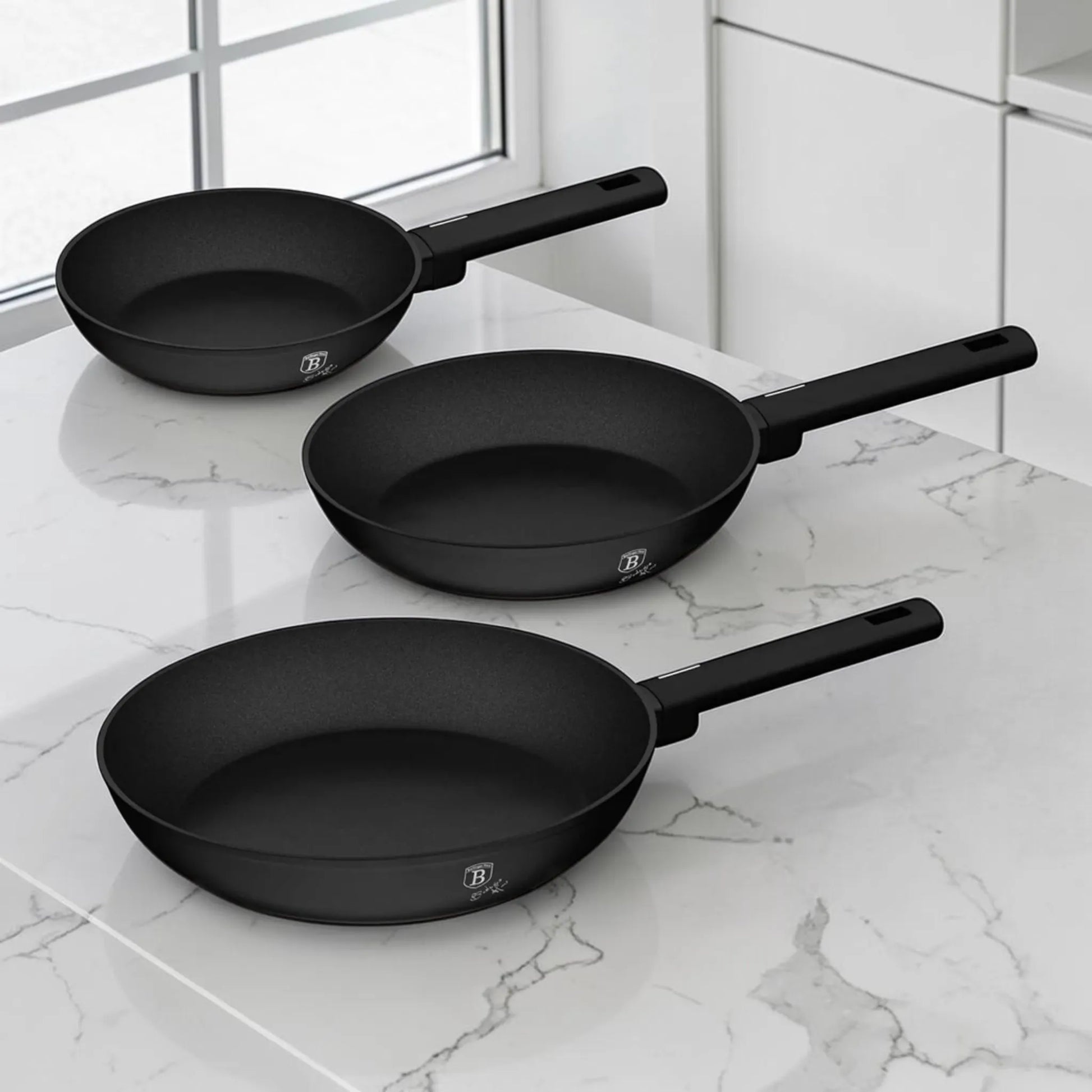Set de 3 sartenes Berlinger Haus BH-8195A negro mate de 20, 24 y 28 cm sobre cocina moderna con superficie de mármol.