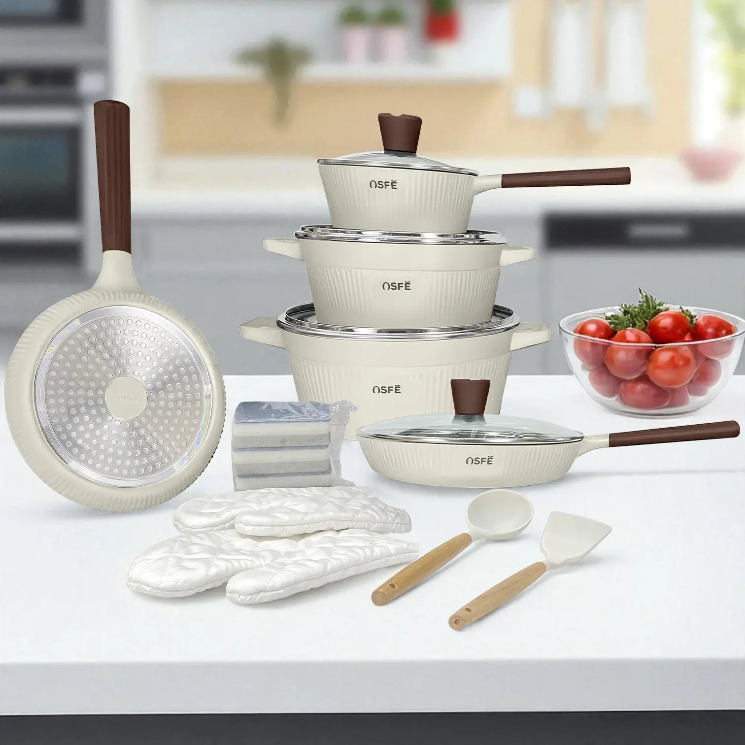 Set de cocina de 16 piezas marca NSFE modelo Athena en color blanco crema, con ollas, sartenes, tapas de vidrio templado, guantes, espátula, cucharón y esponjas, presentado sobre mesa en cocina moderna.