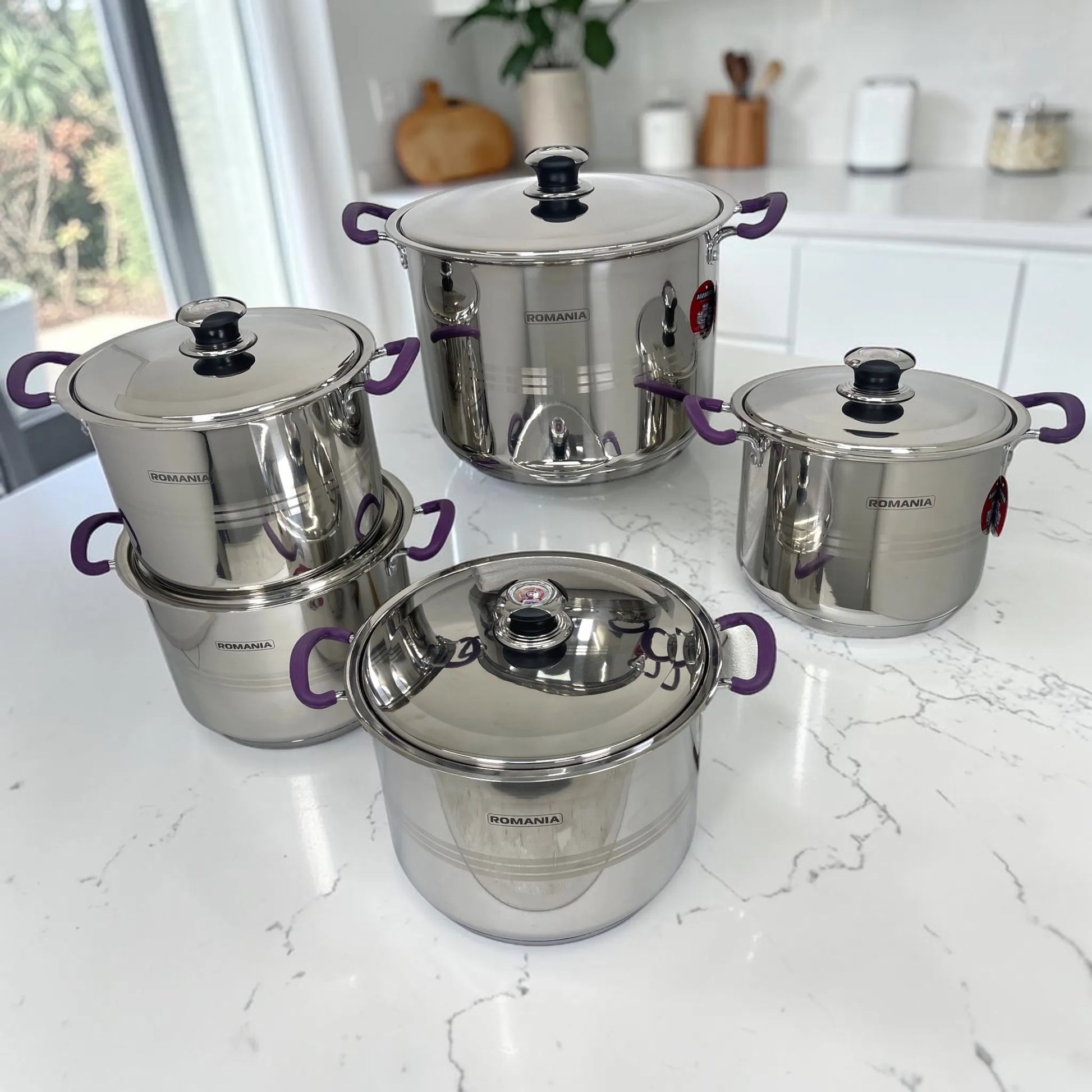 Set completo de ollas Romania con cinco ollas y cinco tapaderas en acero inoxidable, acabado brillante y mangos púrpura.