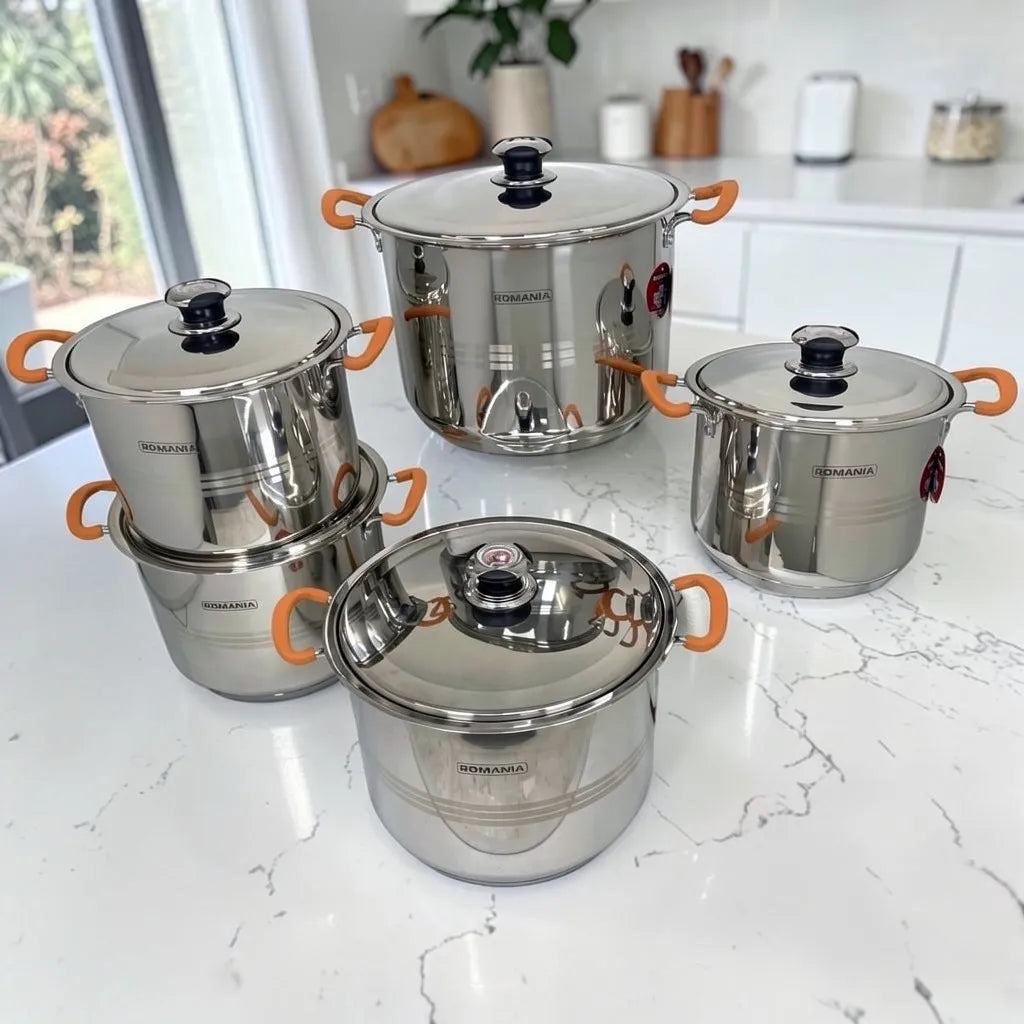 Set completo de ollas Romania con cinco ollas y cinco tapas en acero inoxidable brillante y mangos naranjas, fotografiado sobre encimera blanca.