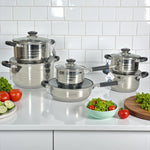 Set de ollas MGFR MR-290G 12 piezas en acero inoxidable 18/10; cacerolas 16, 18, 20 y 24 cm apiladas, sartén 24 cm y cazo 16 cm con tapas de vidrio en cocina blanca.