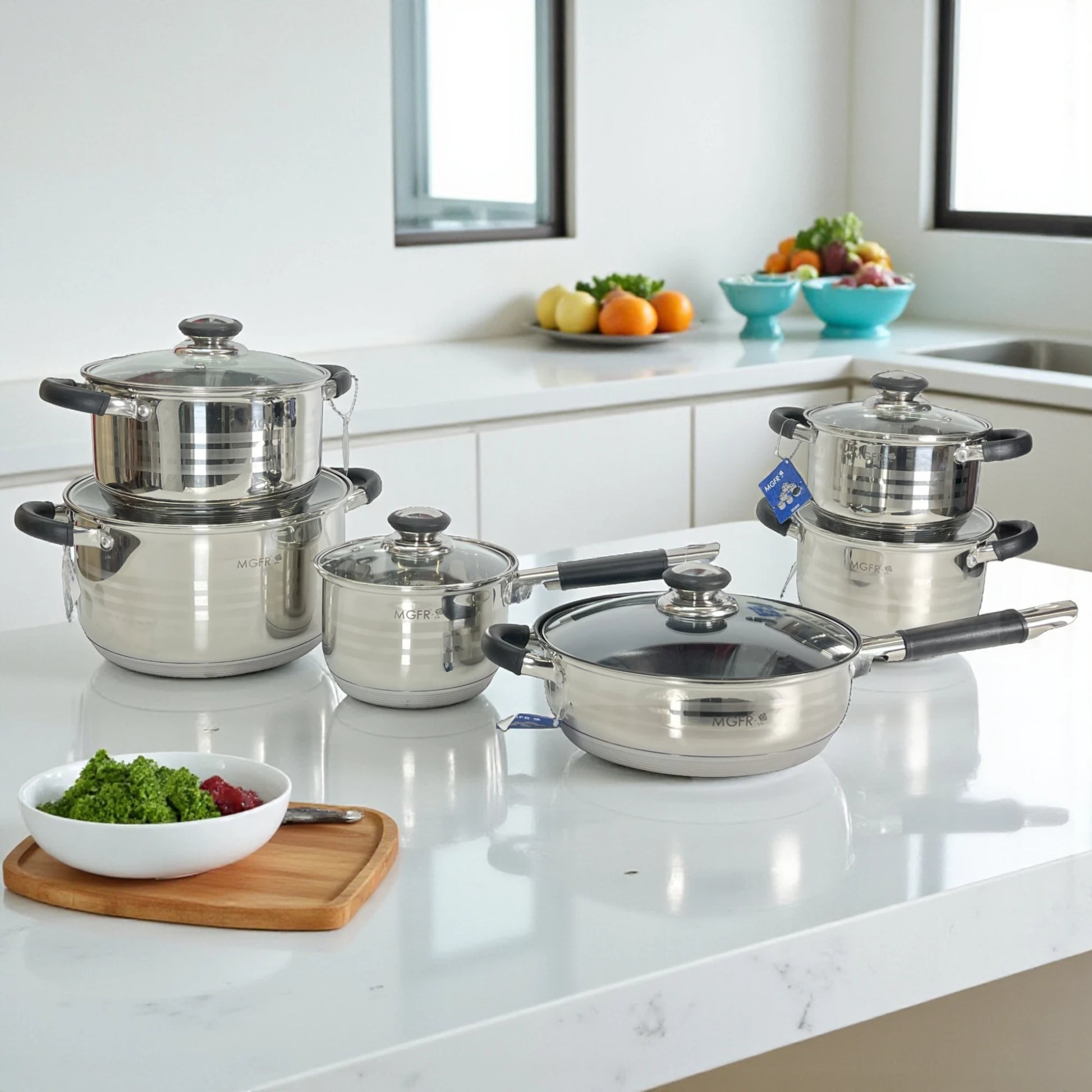Vista de conjunto del set MGFR MR-290G de 12 piezas; ollas de 16, 18, 20 y 24 cm más sartén 24 cm y cazo 16 cm con tapas de vidrio y mangos negros sobre isla de cocina.