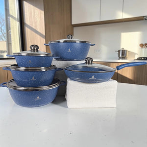 Set de ollas ROCA de 10 piezas color azul granito con tapas de vidrio y sartén en cocina moderna.