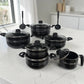 Set de ollas ROCA negro de 12 piezas antiadherente exhibido sobre cocina moderna con tapas de vidrio y utensilios.